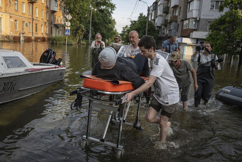 Des bénévoles transportent une femme sur une civière alors qu'elle est évacuée d'un quartier inondé de la rive gauche du Dniepr, à Kherson, juin 2023.