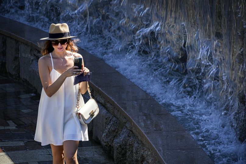 Une femme filme avec un smartphone alors qu'elle se rafraîchit à côté d'une fontaine dans le jardin Alexandre à côté du Kremlin, à Moscou, août 2023