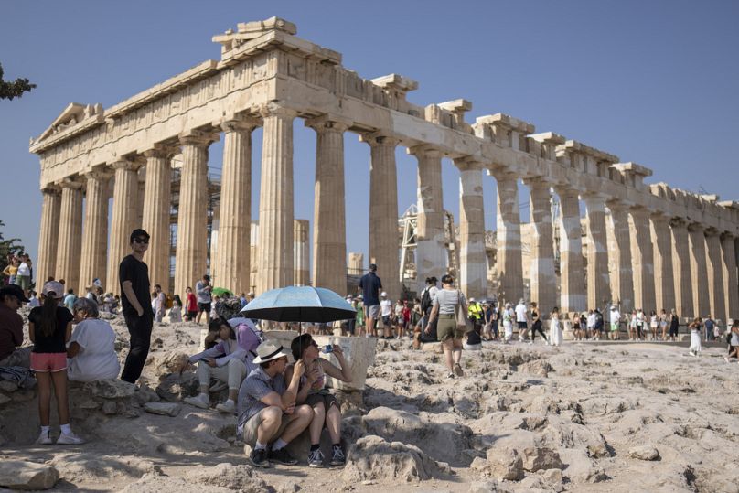 Une touriste boit de l'eau alors qu'elle et un homme sont assis sous un parapluie devant le temple du Parthénon datant de cinq siècles avant JC, sur la colline de l'Acropole, pendant une vague de chaleur, le 13 juillet 2023.