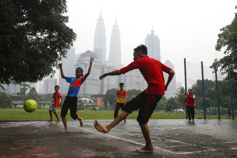 Un jeune Malaisien joue au football contre le bâtiment emblématique de Malaisie, les tours jumelles Petronas, au centre, enveloppé de brume à Kuala Lumpur, en septembre 2015.