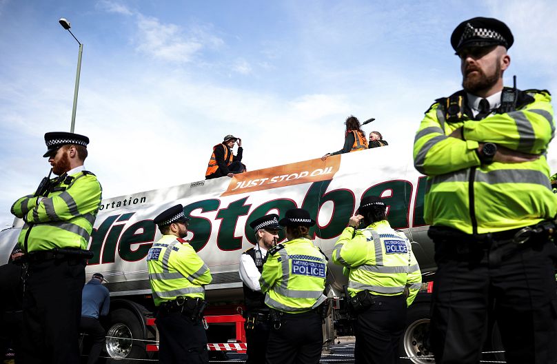Des militants de Just Stop Oil sont assis au sommet d'un camion-citerne de carburant, tandis que des policiers montent la garde, lors d'une manifestation, à un rond-point à l'ouest de Londres, en Grande-Bretagne, le 14 avril 2022.