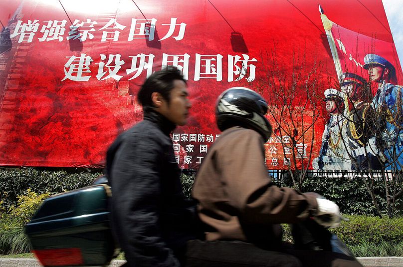 Des hommes roulent à moto devant un slogan du gouvernement en chinois