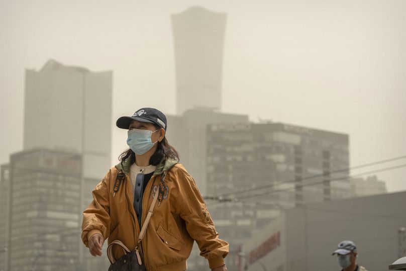 Une femme portant un masque traverse une intersection pendant une tempête de poussière et de sable à Pékin, le mardi 25 avril 2023.