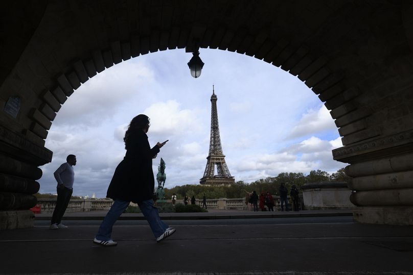 Une femme vérifie son téléphone alors qu'elle marche sur un pont à Paris, novembre 2023