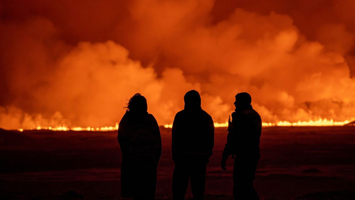 People watch as the night sky is illuminated caused by the eruption of a volcano in Grindavik on Iceland