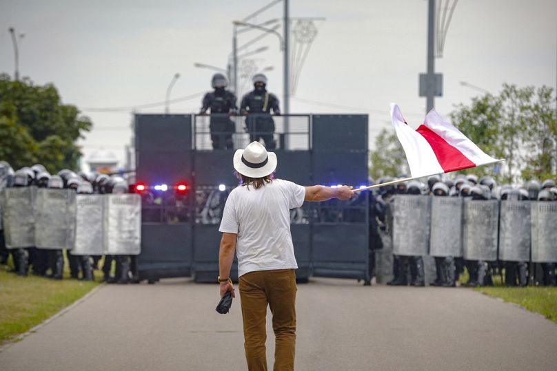 L'artiste Ales Pouchkine brandit un drapeau rouge et blanc devant un blocus policier lors d'une manifestation à Minsk, août 2020.