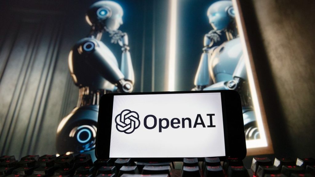The OpenAI logo is seen displayed on a cell phone with an image on a computer monitor generated by ChatGPT