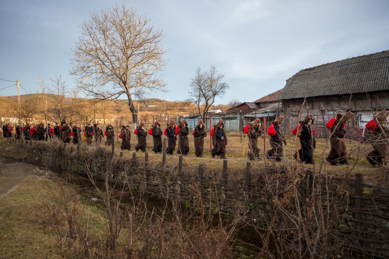 Des membres de la meute d'ours Sipoteni marchent le long d'un ruisseau à Vasieni, dans le nord de la Roumanie, le mardi 26 décembre 2023, tout en visitant les maisons du village pour exécuter la danse rituelle de l'ours.