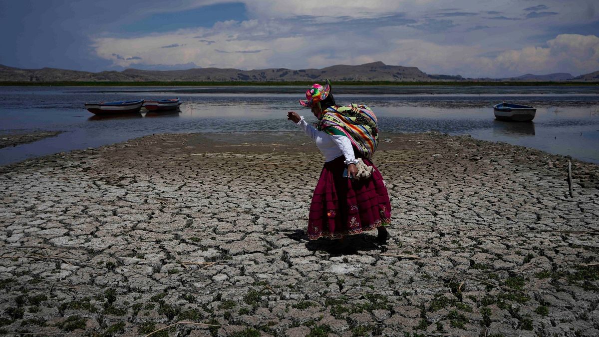 A woman walks on a dried out portion of Lake Titicaca in Coata, Peru, 29 November 2023, during a heat wave.