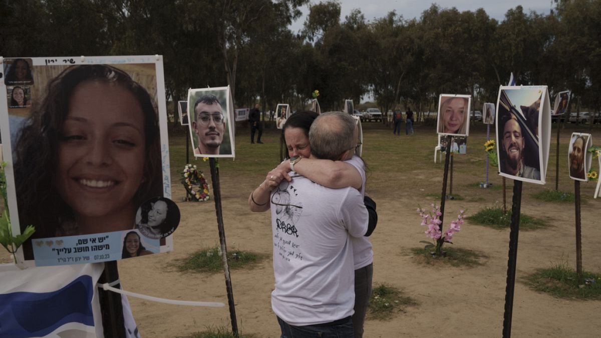 Ela Bahat embraces her husband Idan as they stand next to a picture of their 30-year-old son Dror, right, who was killed on Oct. 7 at the Nova music festival.