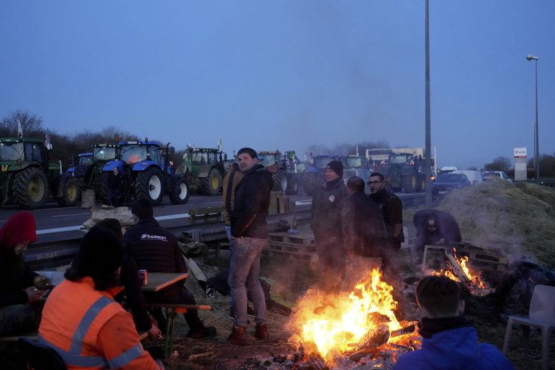 Des agriculteurs se réchauffent autour d'un feu de joie alors qu'ils bloquent une autoroute avec leurs tracteurs, à Ourdy, au sud de Paris, mercredi.