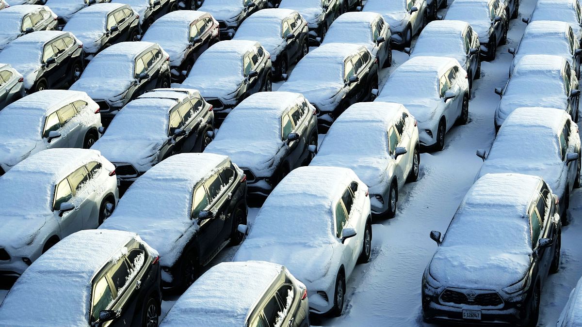 Snow covered vehicles sit in a rental car parking lot at the O