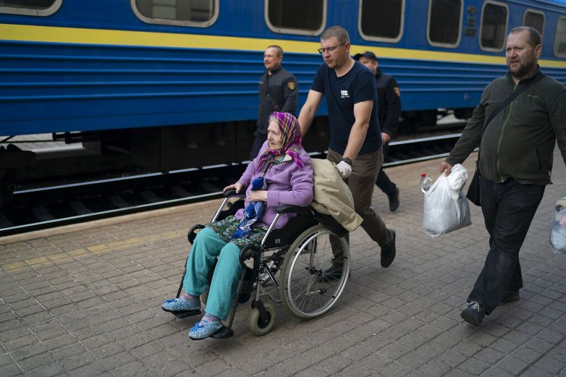 Des bénévoles aident une femme âgée à monter à bord d'un train fuyant la guerre à Severodonetsk et dans les villes voisines, dans une gare de Pokrovsk, avril 2022
