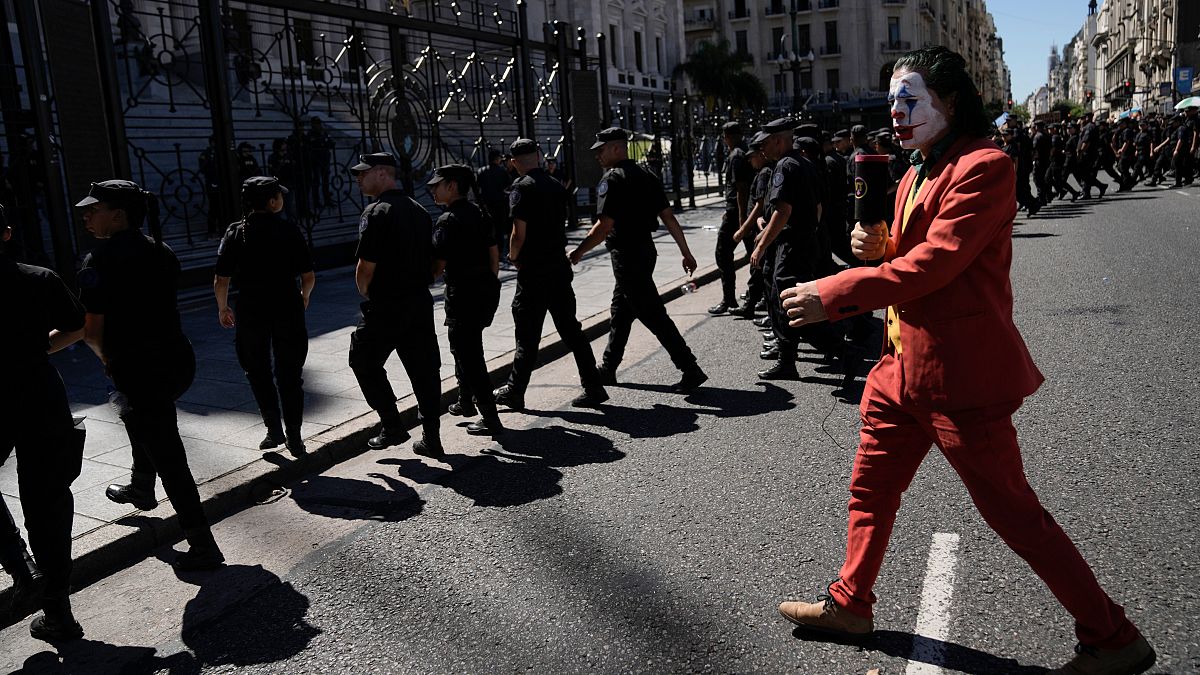 A protester in a Joker costume walks behind police leaving the area near Congress at the end of a protest during a national strike in Buenos Aires,