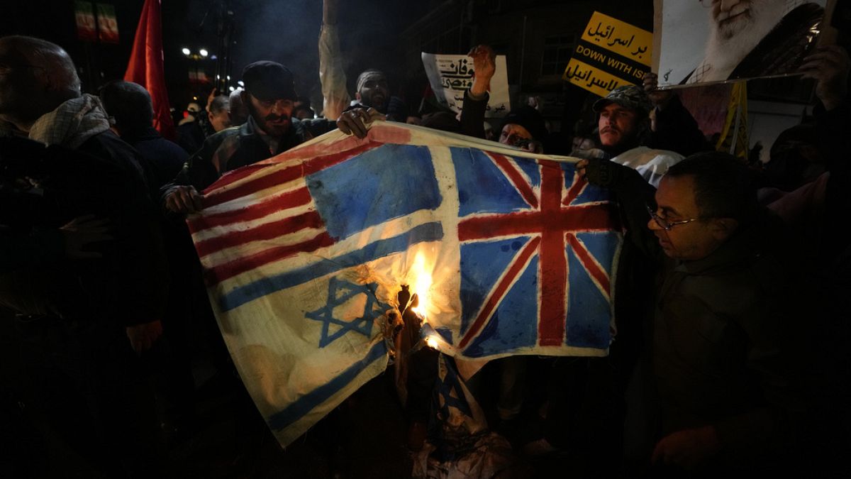 Iranian demonstrators burn representations of British, U.S. and Israeli flags during a protest, in front of the British Embassy in Tehran, Iran, Friday, Jan. 12, 2024.