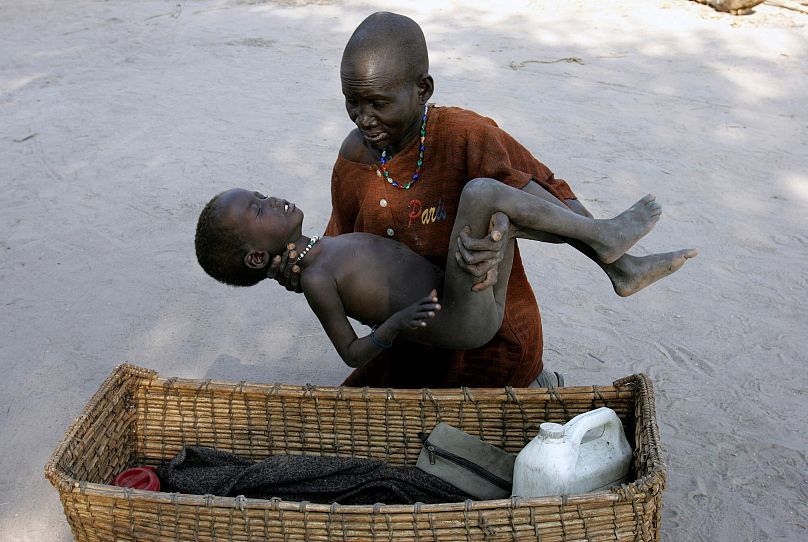 Une mère place délicatement son fils dans un panier alors qu'elle l'emmène dans une clinique de Médecins Sans Frontières après qu'il ait contracté le paludisme, à Lankien, au Sud-Soudan, en 2005.