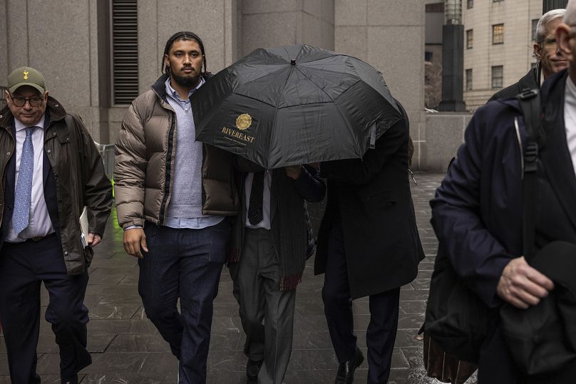 Joe Lewis, au centre, quitte le tribunal fédéral de Manhattan sous le couvert d'un parapluie après avoir plaidé coupable à des accusations de délit d'initié, le mercredi 24 janvier 2024.