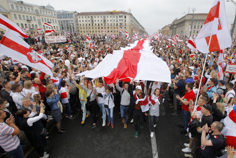 Des manifestants brandissent un immense drapeau historique de la Biélorussie alors que des milliers de personnes se rassemblent pour manifester sur la place de l'Indépendance à Minsk, en 2020.