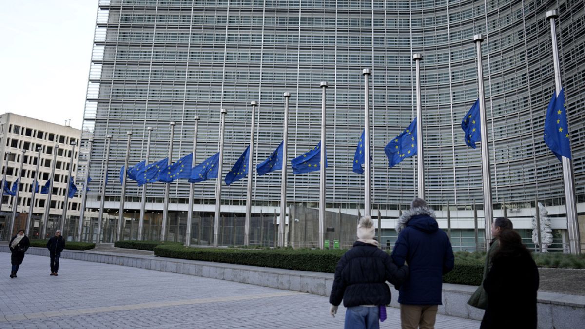 Pedestrians walk past as European Union flags flap in the wind at half staff, in remembrance of former European Commission President Jacques Delors, in front of European Union