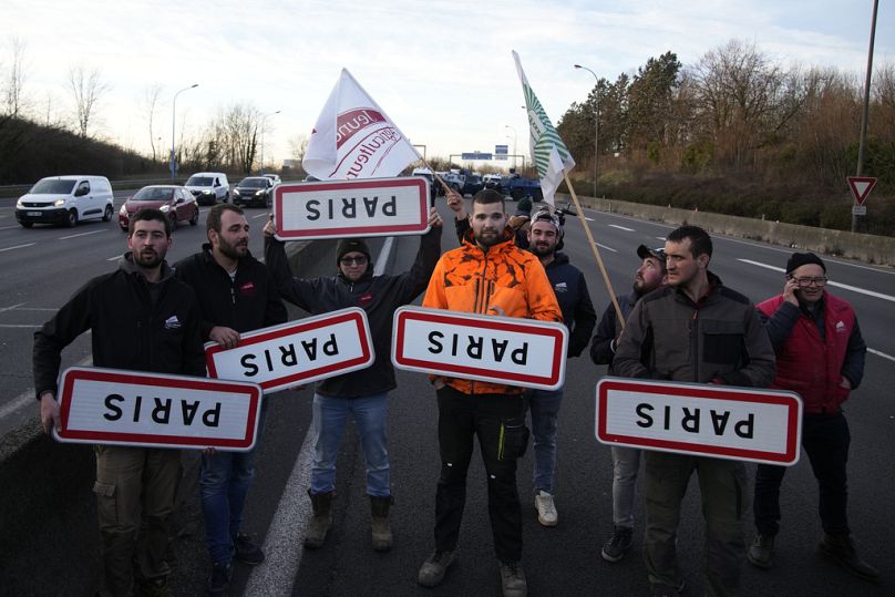 Des agriculteurs tiennent des panneaux routiers à l'envers indiquant Paris sur une autoroute bloquée, le mercredi 31 janvier 2024 à Chilly-Mazarin, au sud de Paris.
