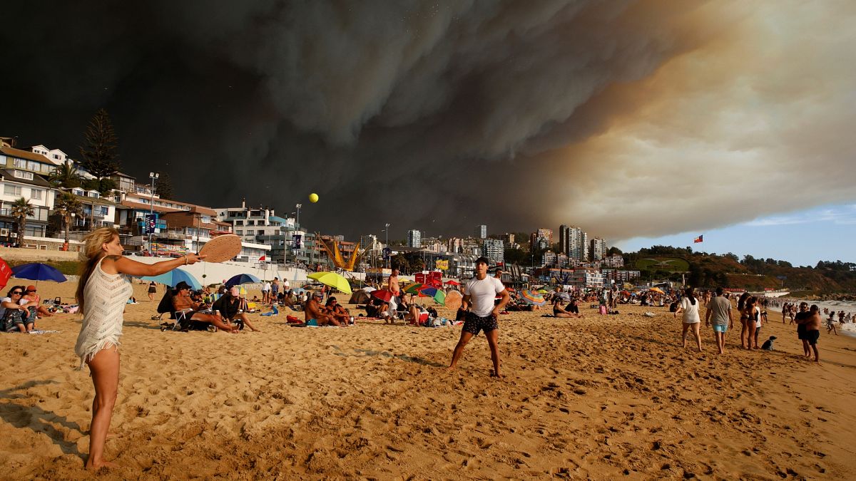 Vacationers play paddle ball on the beach backdropped by a darkening sky caused by smoke from nearby forest fires in Viña del Mar, Chile.