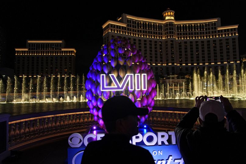 Les gens se tiennent près de la signalisation pour le Super Bowl alors que les fontaines du Bellagio entrent en éruption le long du Strip de Las Vegas avant le Super Bowl