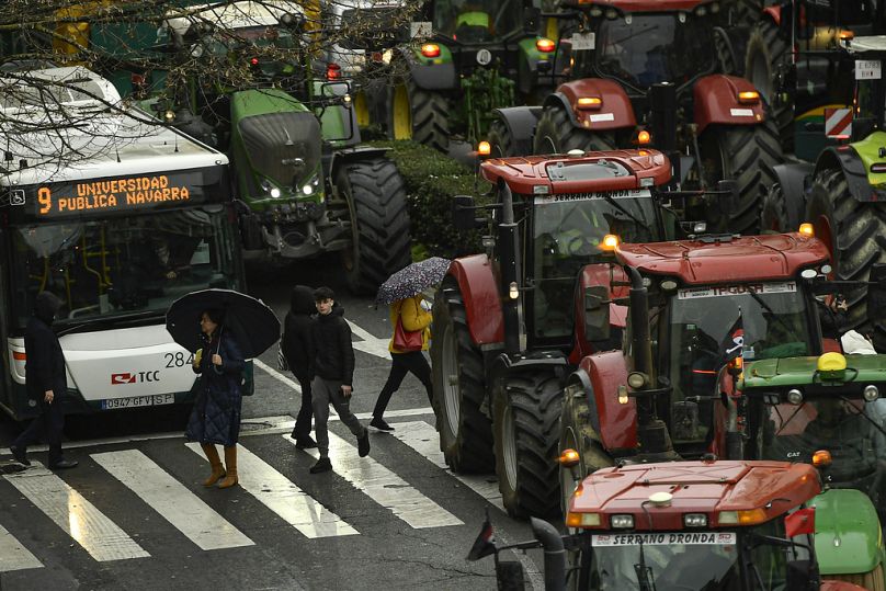 Des piétons traversent la route tandis que des agriculteurs avec leurs tracteurs défilent le long du centre-ville tout en participant à une manifestation, à Pampelune, en février 2024.