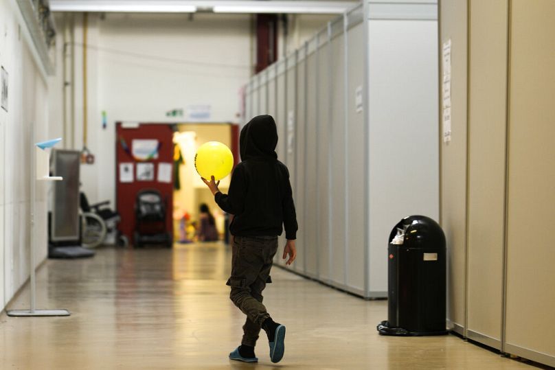 Un garçon avec un ballon marche à côté d’unités de couchage de fortune à l’intérieur du refuge temporaire pour réfugiés de l’ancien aéroport de Tegel à Berlin, en Allemagne, le 9 novembre 2022.