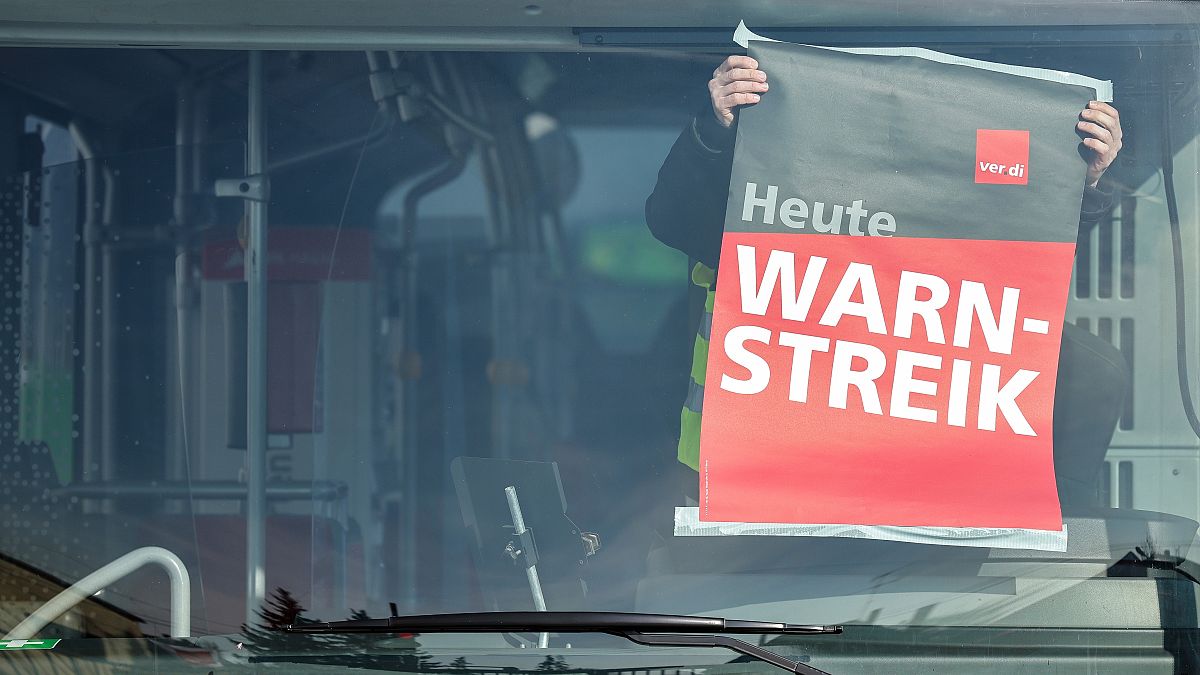 An employee of Hallesche Verkehrs-AG (HAVAG) attaches a strike poster in the window of a bus, at a depot, in Halle, Germany, Thursday, Feb. 29, 2024.