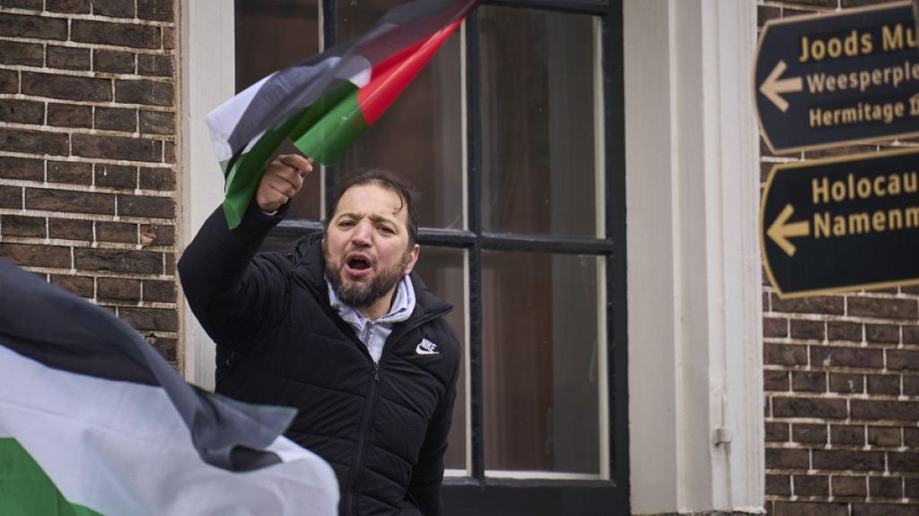 A man waves a Palestinian flag next to signs for the Holocaust Monument and the Jewish Museum as demonstrators protested against Israel