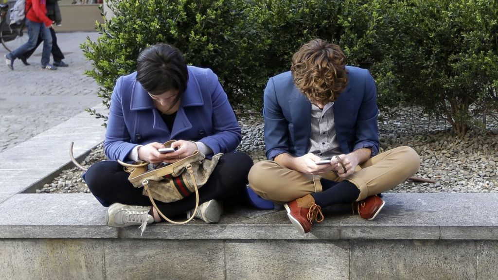 A young man and woman check their smart phones as they sit on a wall in Milan, Italy.