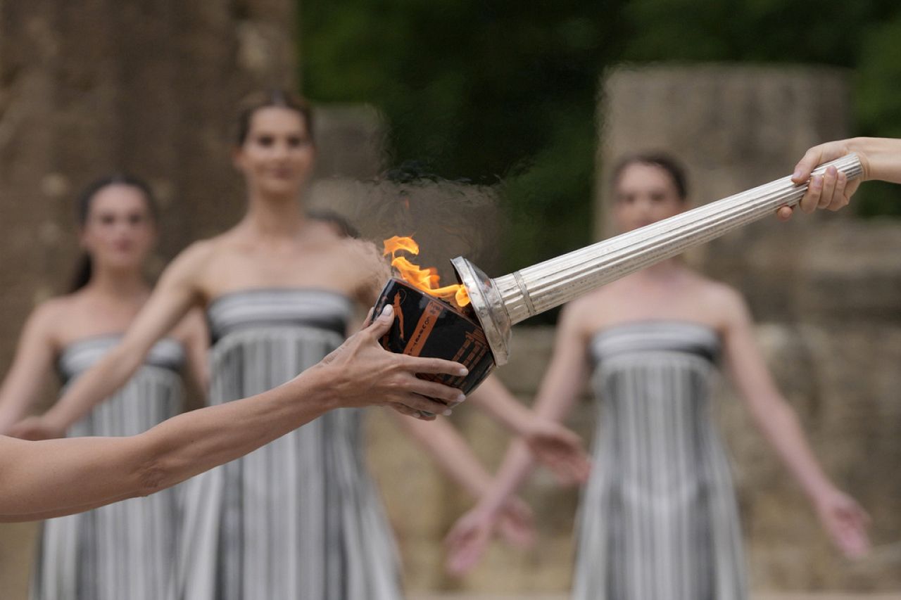 L'actrice Mary Mina, jouant le rôle de la grande prêtresse, à droite, allume une torche lors de la cérémonie officielle d'allumage de la flamme des Jeux olympiques de Paris.