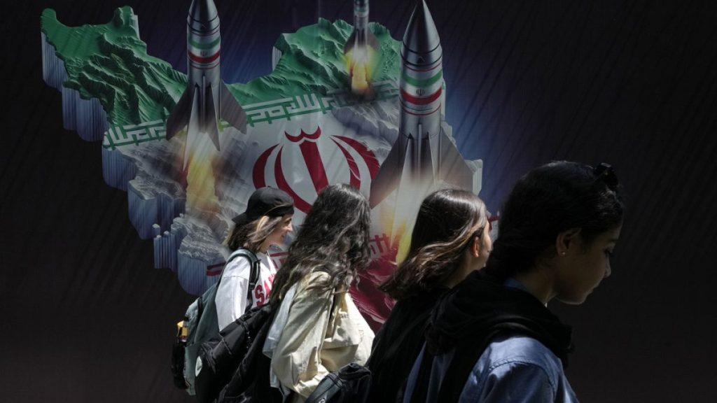 Women walking past banner showing missiles being launched from Iranian map