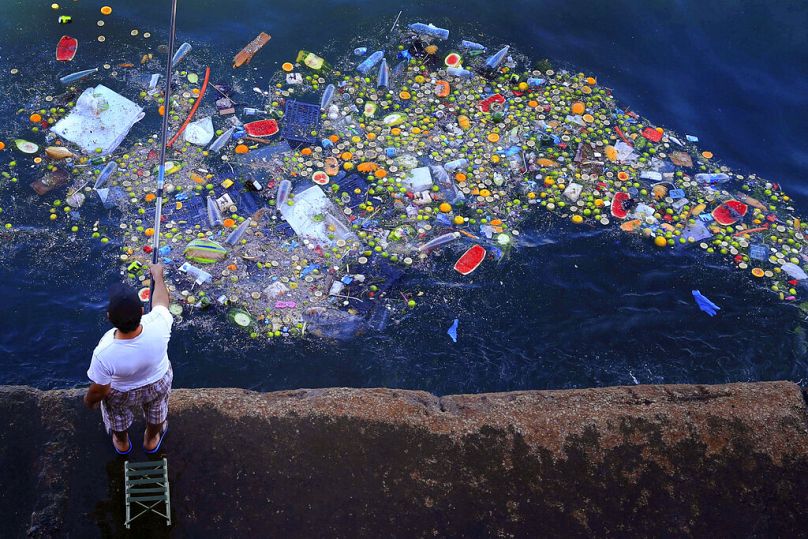 Un homme tient une canne à pêche alors que des déchets flottants heurtent le littoral de la mer Méditerranée, à Beyrouth, en septembre 2016.