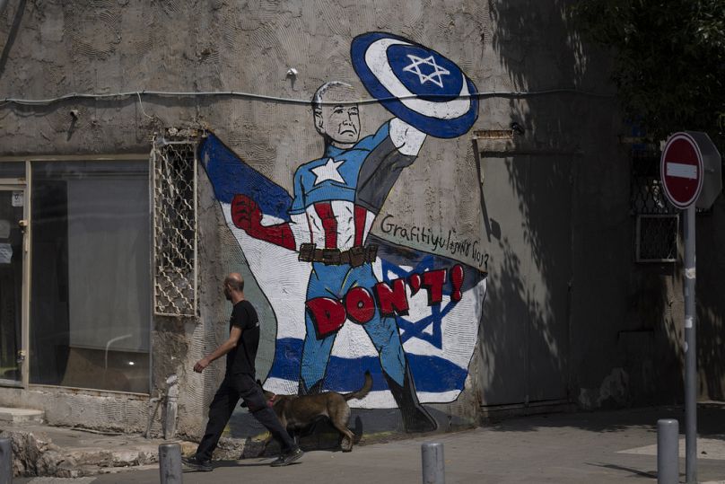 Un homme passe devant une fresque représentant le président américain Joe Biden comme un super-héros défendant Israël dans une rue de Tel Aviv, avril 2024.