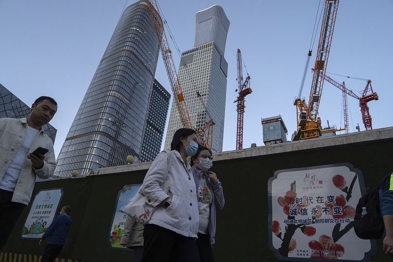 Des femmes portant des masques passent devant des grues de construction près du quartier central des affaires de Pékin, le mardi 16 avril 2024.