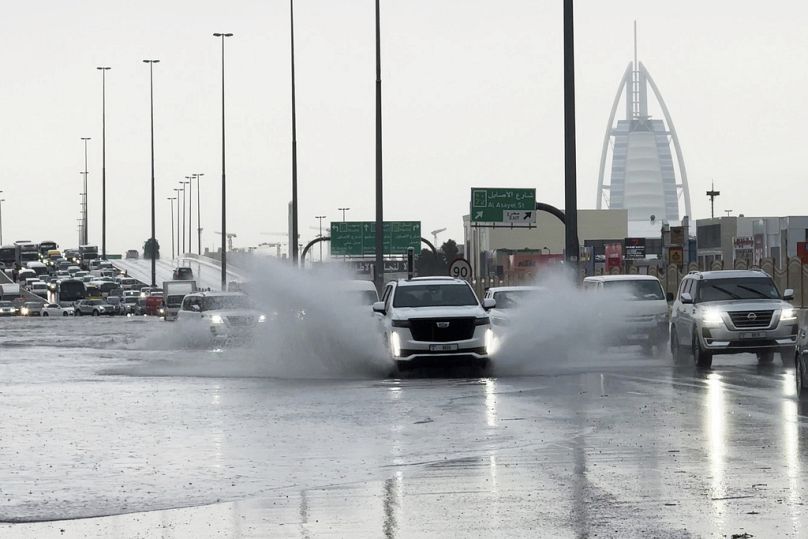 Un SUV éclabousse l’eau stagnante sur une route de Dubaï, avec l’hôtel de luxe Burj Al Arab en arrière-plan.  à Dubai
