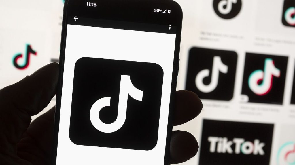 The TikTok logo is displayed on a mobile phone in front of a computer screen.