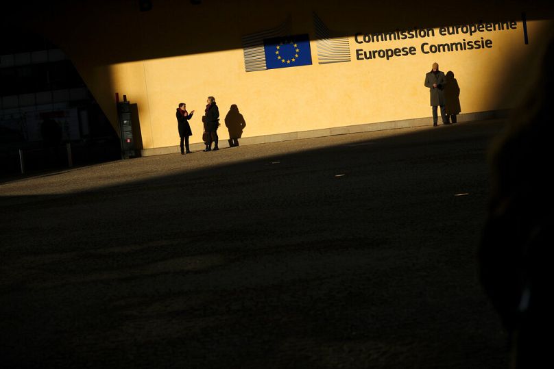 Des gens se tiennent sous le soleil à l’entrée du siège de la Commission européenne à Bruxelles, décembre 2019