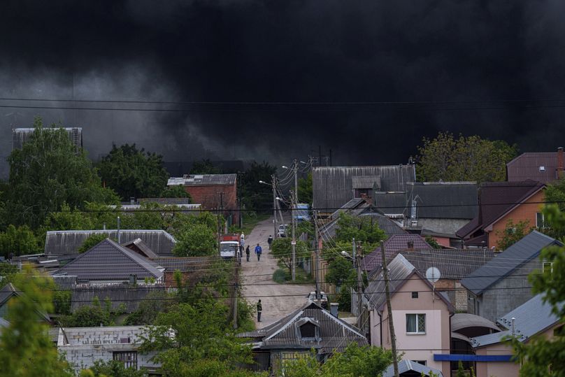 Des gens marchent dans une rue tandis que la fumée s'élève après une attaque russe à Kharkiv, en Ukraine, le vendredi 17 mai 2024.