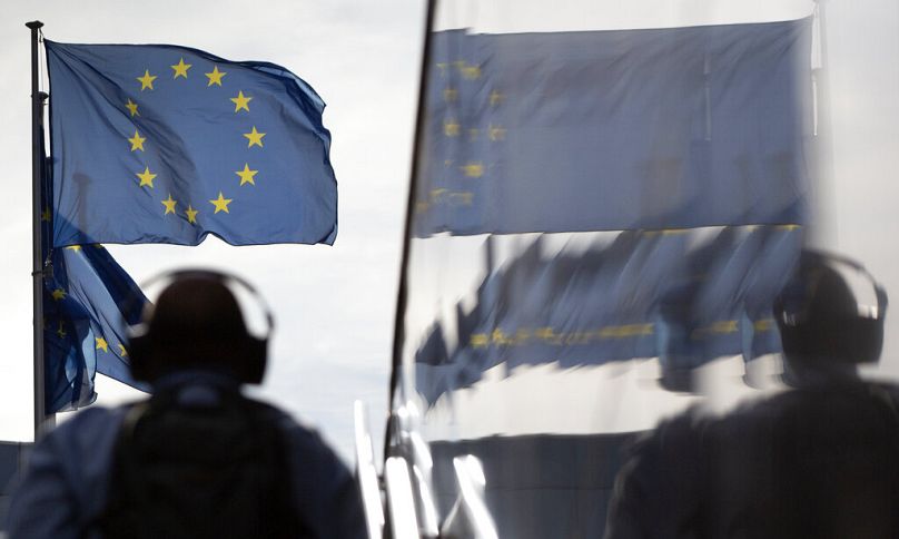Un homme portant des écouteurs se dirige vers les drapeaux de l'UE alors qu'il se reflète dans le marbre du bâtiment de la Commission européenne à Bruxelles, en août 2020.