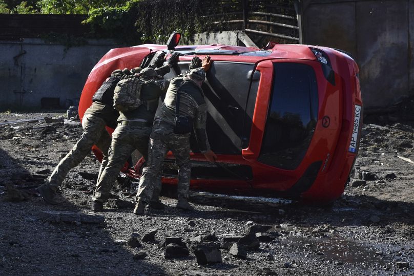Des militaires ukrainiens retournent une voiture endommagée sur les lieux d'une attaque de missile russe à Zaporizhzhia.