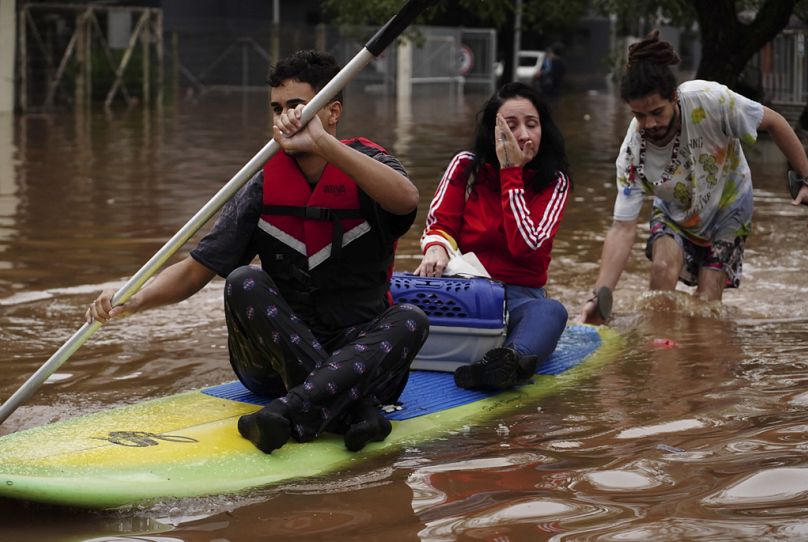 Des gens évacuent sur une planche de surf un quartier inondé par de fortes pluies, à Canoas, dans l'État de Rio Grande do Sul, au Brésil