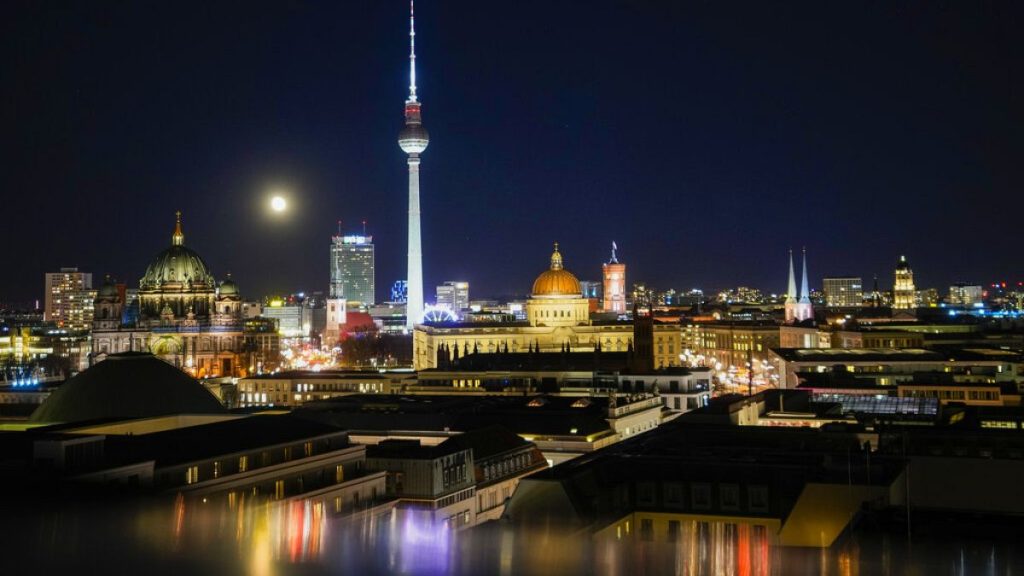 The moon rises over the illuminated skyline of the German capital in Berlin, Germany, Monday, Nov. 22, 2021.