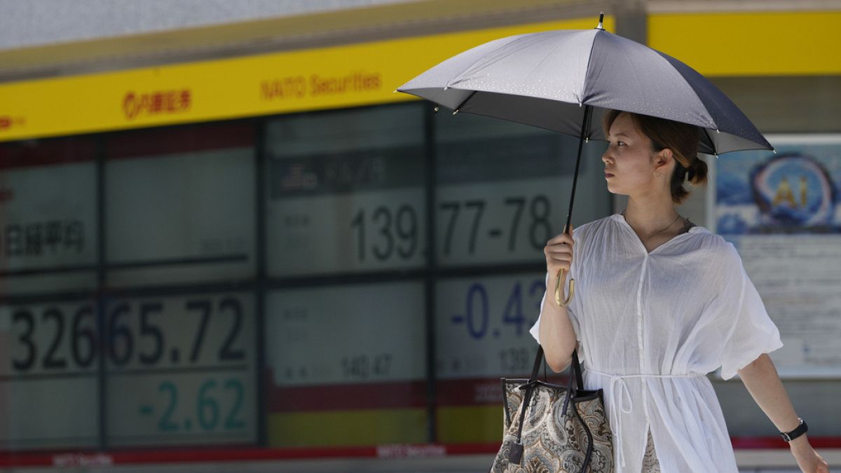 A woman walks across an intersection near monitors showing Japan