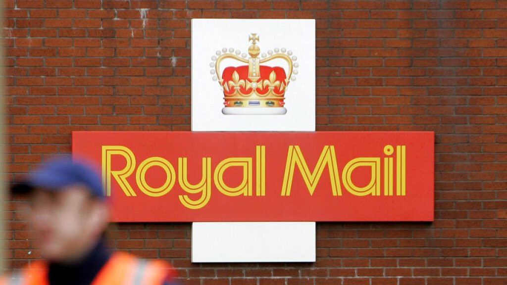 A British Royal Mail logo is seen behind a postal worker walking at a delivery office in London, Monday, Oct. 19, 2009.