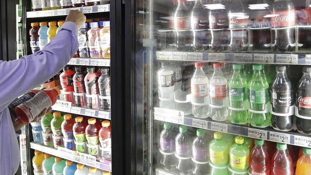 A shop owner reaches into a drink display refrigerator.