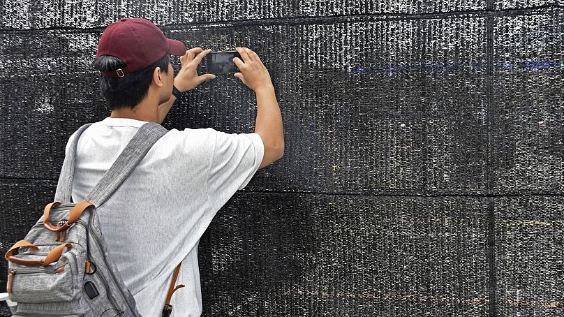 Un visiteur tente de prendre une photo à travers un trou sur un écran noir installé en face d'un dépanneur à Fujikawaguchiko, au Japon, le 24 mai 2024.