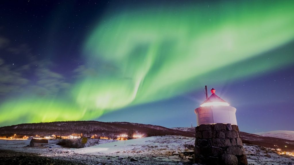 Aurora borealis or northern lights are visible in the sky above a lighthouse to the village of Strand near Tromso in northern Norway.
