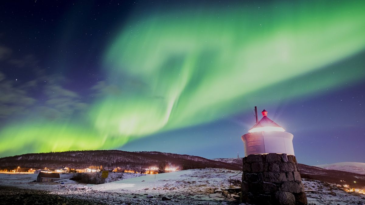 Aurora borealis or northern lights are visible in the sky above a lighthouse to the village of Strand near Tromso in northern Norway.